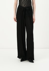 Pantalones anchos negros con una textura suave, con una cintura atada y un diseño fluido. Combinados con una blusa de encaje negra.