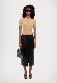 Beige ribbeskjorte med korte ermer og knappedetaljer, svart skinn midiskjørt, svarte block-heeled sandaler, og en liten svart håndveske.