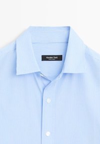 Chemise bleu clair avec fines rayures verticales blanches, col pointu et boutons blancs, étiquetée Massimo Dutti, fabriquée en Turquie.