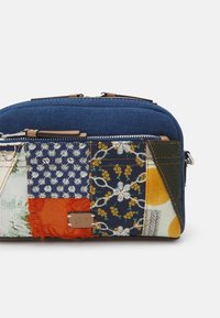 Patchworková zipová taštička kombinující modrý denim a různé vzorované látky v oranžové, žluté a květinové designy. Součástí jsou kožené detaily.