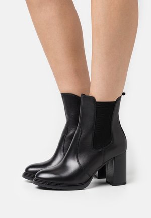 Bottines en cuir noir à finition lisse, munies de panneaux latéraux élastiques, d'un talon bloc et d'un bout arrondi.