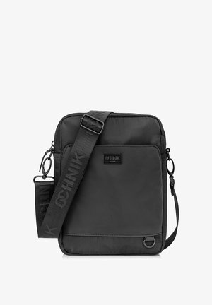 Czarna torba crossbody wykonana z gładkiego nylonu w kształcie prostokąta. Posiada markowy pasek, zamek błyskawiczny oraz detal w postaci bocznego pierścienia.