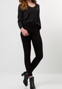 Camicetta nera a maniche lunghe abbinata a jeans neri aderenti e stivali alla caviglia. Tessuto morbido, vestibilità slim e leggero lucido sulla camicia.