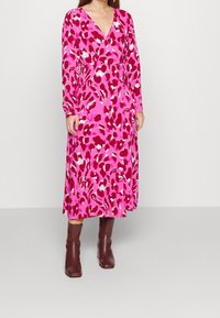 Fuchsia long-sleeve dress with a v-neck, featuring a leopard print pattern in shades of red and white. Worn with brown ankle boots.