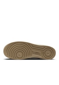 Sole tenisky Nike v světle hnědé gumě, s kruhovými a vlnitými vzory běhounu, se středovou kruhovou výčnělkem a vyraženým logem.