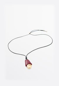 Collana con cordoncino nero e chiusura regolabile, con pendente in oro parzialmente coperto da un pezzo di pelle rossa scuro piegato.