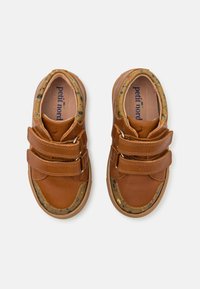 Zapatos de piel marrón con dos tiras de Velcro, diseño de puntera redonda y acentos moteados a lo largo de la suela, que proporcionan un acabado texturizado.
