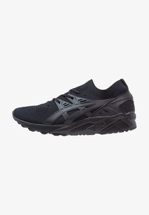 Zapatilla deportiva negra con parte superior de punto, cierre de cordones y suela con textura, con detalle de logotipo lateral y entresuela acolchada.
