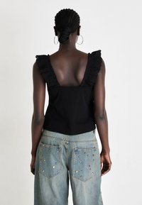 Black sleeveless top with ruffled, lace-trimmed shoulders; paired with light blue jeans featuring decorative metallic embellishments on pockets.