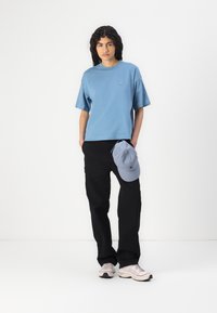 Blue cotton T-shirt with short sleeves and round neckline, paired with black loose-fitting pants. Includes light blue cap resting on pants.