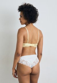 Lace bralette in pale yellow with adjustable straps; white panties with lace trim at the back, showcasing a smooth fabric texture.
