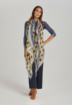 Foulard triangulaire vert et bleu à pois rouges, bords à franges, tissu léger drapé sur les épaules d'un modèle.