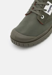 Sneaker verde din cauciuc, cu un superior texturat, vârf întărit, accente portocalii contrastante și șireturi rotunde cu ochiuri din metal.