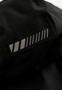 Tessuto nero con una sottile trama a griglia presenta un motivo riflettente argento di forme geometriche lungo la parte superiore, creando un dettaglio moderno.