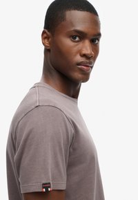 Kortærmet, crew-neck t-shirt i grå bomuld, med et lille mærke på venstre ærme i rød, hvid og grøn.