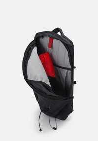 Zaino nero con interno grigio, dotato di una piccola borsa con cordino rossa all'interno e corde di regolazione alla base. Apertura con zip.