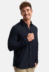Camisa de manga larga en color marino, hecha de un tejido suave, con cuello abotonado, que cuenta con un panel frontal y un logo sutil en el pecho.