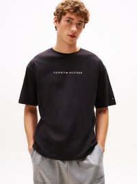 T-shirt en coton noir avec un logo central blanc. Manches courtes et coupe décontractée. Pantalons de survêtement gris avec poches latérales. Design simple.