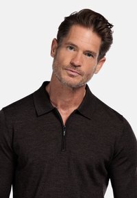 Dunkelbraunes Langarm-Polohemd mit Reißverschlusskragen. Hergestellt aus weichem, strukturiertem Stoff. Schlanke Passform mit dezenten Steppnähten.