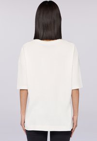 T-shirt bianco oversize con maniche corte, scollatura rotonda e retro senza cuciture. Il tessuto appare morbido con una texture liscia.