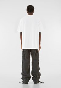 Hvid oversized t-shirt med korte ærmer, parret med løse sorte cargobukser med sidelommer og snor i kanten.