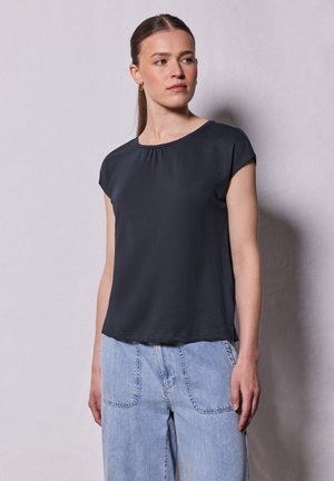 Zwart shirt met korte mouwen en een ronde halslijn, met een geplooid detail aan de voorkant. Zachte stof met een comfortabele pasvorm, gecombineerd met lichtblauwe jeans.