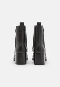 Bottes basses noires avec une tige en cuir lisse, un bout arrondi, des panneaux latéraux élastiques et un talon bloc. Deux languettes de tirage à l'arrière.