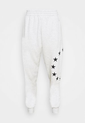 Vaaleanharmaa huppari ja siihen sopivat pehmeästä kankaasta tehdyt joggers-housut, joissa on logo ja housuissa mustat tähtikoristeet. Mustat nilkkurit viimeistelevät asun.