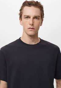 Tricou negru cu mânecă scurtă dintr-un material tricotat texturat, cu guler rotund. Design minim, fără modele sau accente vizibile.