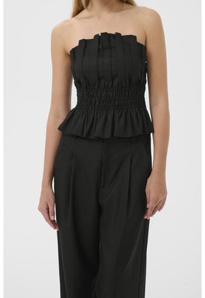 Haut noir sans bretelles avec des détails plissés, taille froncée et ourlet à volants porté avec un pantalon noir ample sur une personne debout.