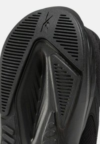 Semelle de chaussure de sport noire en caoutchouc texturé avec des rainures et des accents pour une traction améliorée, offrant adhérence et flexibilité.
