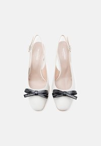 Witte slingback schoenen met een ronde neus, voorzien van een zwarte laks strik en logodetail aan de voorkant. Gladde textuur en strak ontwerp.