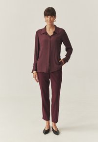 Camisa de botones burdeos con rayas verticales y cuello puntiagudo, combinada con pantalones slim-fit a juego. Zapatos negros de punta.