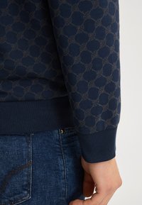 Felpa blu navy con un motivo testurizzato di cerchi intrecciati in una tonalità più chiara, con polsini e fondo a costine per una vestibilità aderente.