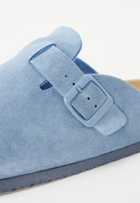 Svijetloplavi suknjeni slip-on cipele s širokom trakom i podesivom kopčom. Imaju meku teksturu i dizajn oblikovanog uloška.
