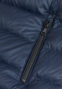 Marineblaue Steppjacke mit gesteppte Paneele, glatter Textur und einem schwarzen Reißverschluss mit einem Gummizuglaschen an der Seite.