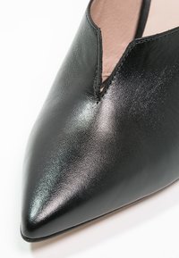 Chaussure noire en cuir à bout pointu avec une découpe en forme de V sur le bord supérieur et une finition lisse et brillante.
