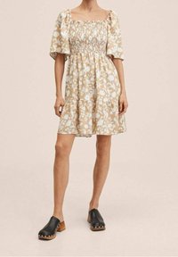 Robe à imprimé floral beige avec manches ballon et corsage froncé. Sabots noirs avec talons en bois et accents argentés.