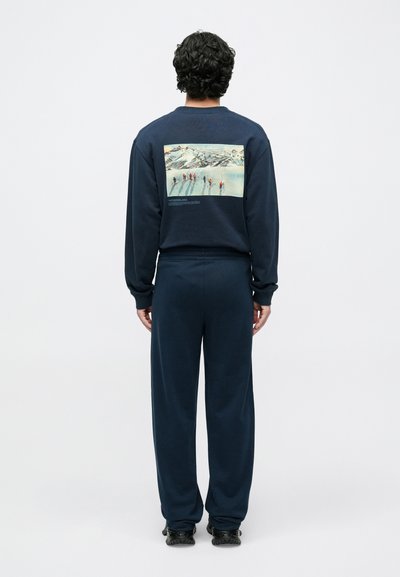 Zestaw z ciemnogranatowej bluzy i spodni, wykonany z miękkiego materiału, z kolorowym obrazem narciarzy na ośnieżonym tle na plecach. Luźny krój, ściągacze na rękawach.