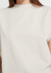 Kermaviininvärinen puuvillapaita, jossa on korkea kaulus, rento malli ja lyhyet hihat. Liukas pinta, yksinkertainen muotoilu ilman näkyviä kuvioita.