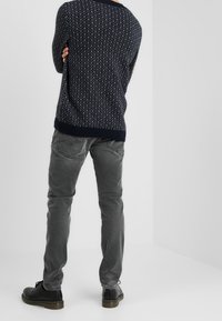 Tmavě modrý pletený svetr se vzorem diamantů, doplněný šedými kalhotami. Černé boty dokončují outfit a vytvářejí neformální vzhled.