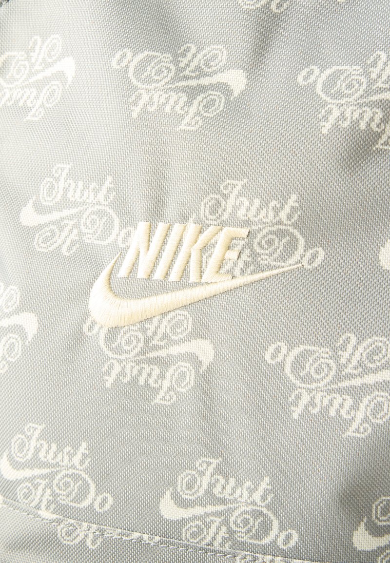 Hellgrauer Stoff mit wiederholtem weißen Schriftzug „Just Do It“ und Nike-Swoosh, mit einem auffälligen bestickten weißen „NIKE“-Logo und Swoosh.