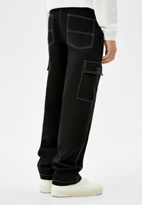 Svarta cargobyxor med vit sömnad, som har flera fickor och avslappnad passform. Matchade med vita sneakers för kontrast.