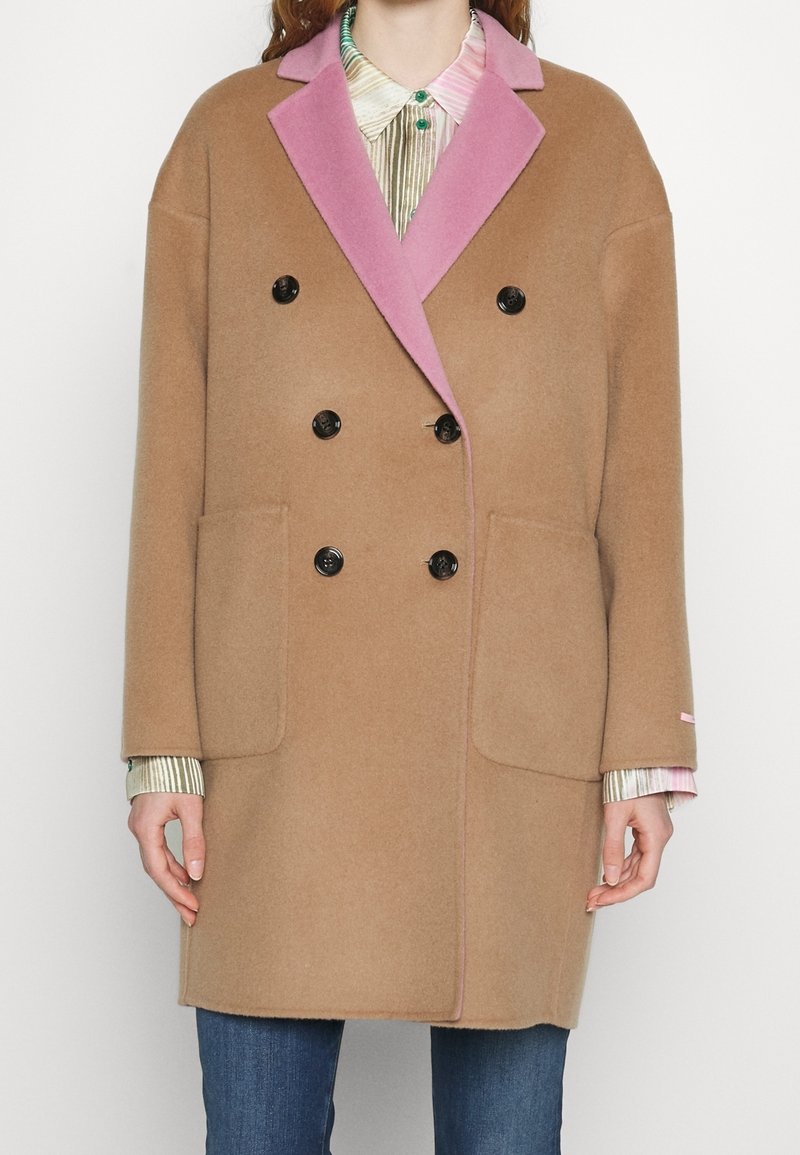 Dubbelbreasted jas van camel wol met een roze kraag. Bevat zwarte knopen en twee vo pockets. Gstyled over een gestreept overhemd.