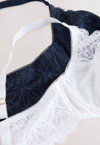 Soutiens-gorge en dentelle noirs et blancs, ornés de motifs floraux et de bretelles réglables, posés à plat sur un fond neutre.