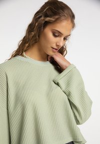 Maglione a coste in un verde chiaro, con una vestibilità ampia, collo rotondo e polsini larghi. Presenta un design rilassato, adatto per un abbigliamento casual.