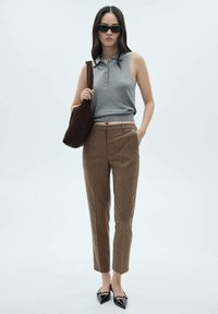 Graues ärmelloses Poloshirt, braune karierte Hose und schwarze spitze Ballerinas. Als Accessoires dienen eine dunkelbraune Umhängetasche und Sonnenbrille.