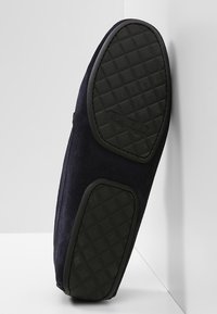 Semelle de chausson en cuir noir avec une surface texturée, arborant un motif matelassé. Le design est minimaliste avec des bords arrondis et sans marque visible.