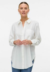 Hvid skjorte med knaplukning og krave, lange ærmer og en brystlomme; let, glat stof med en let løs pasform.