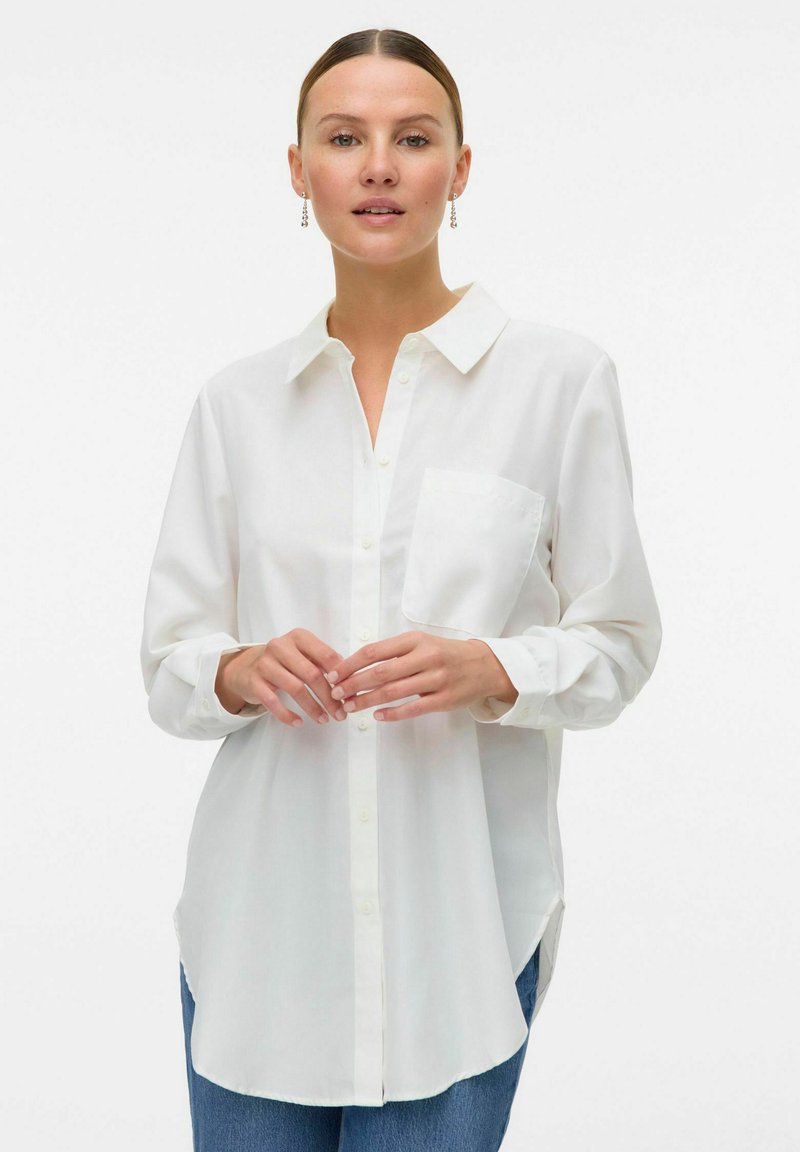 Hvid skjorte med knaplukning og krave, lange ærmer og en brystlomme; let, glat stof med en let løs pasform.